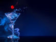 cherry falling into martini cocktail splashing in blue smoky background