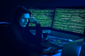 Wall Mural - Hacker in mask using computer in dark room