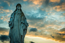 Old Grungy And Worn Statue Of Jesus In A Cemetery At Sunset