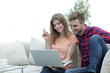 © ASDF - young man with his girlfriend watching a TV show on the laptop sitting in the living room