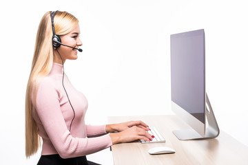 Portrait of a smiling blonde businesswoman with headset working with computer on white