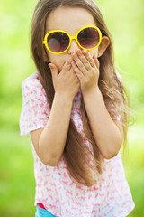 Wall Mural - Kids fashion and accessory concept. Portrait of smiling cute little girl in trendy eyewear. Windy summer day. Outdoor shot