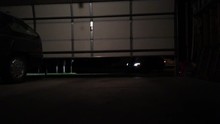 Car Entering Garage With Lights On And Approaching All The Way Up To Camera Before Shutting Off Headlights.   