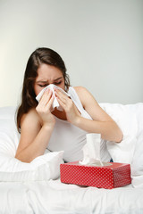 Wall Mural - Sick young woman sneezing in tissue in white bed