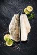  Fresh fish,  raw cod fillet with addition of herbs and lemon slices on black stone background, top view