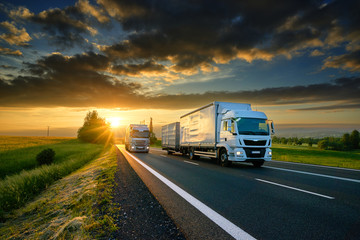 Wall Mural - overtaking trucks on an asphalt road in a rural landscape at sunset