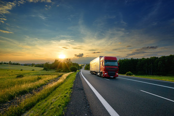 Red truck driving on the asphalt road in rural landscape at sunset