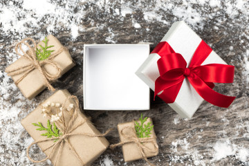 Open and blank white gift with red ribbon bow on wooden background with wrapped brown craft handmade boxes and snow.