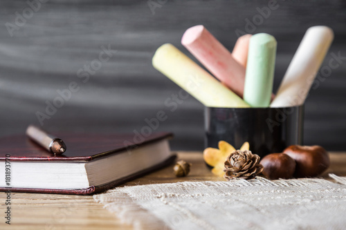 Fotografie, Obraz Teacher's colorful chalks with school journal and pen on the wooden table at the blackboard in classroom