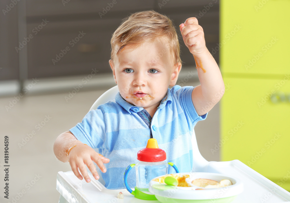 Adorable baby eating while sitting in highchair at home