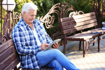 Wall Mural - Handsome mature man with tablet on bench in park