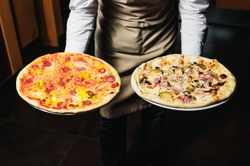 Waiter carrying two different plates with a tasty pizza. Photo with two pizza. Pizza with mushrooms and pizza with salami. Italian food. Italian restaurant.