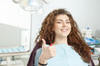 © Sokirlov - Young female patient visiting dentist office.Beautiful smiling woman with healthy straight white teeth sitting at dental chair and making thumbs up.Dental clinic.Stomatology