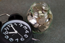 Alarm Clock And Step Of Coins Stacks With Coin In Glass Jar On Working Table, Time For Savings Money Concept.