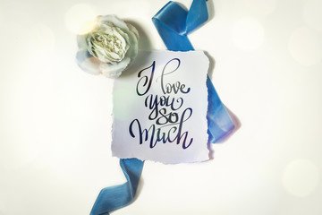 Wall Mural - Rose and blue ribbon on a white background. Inscription I love you so much. Bokeh