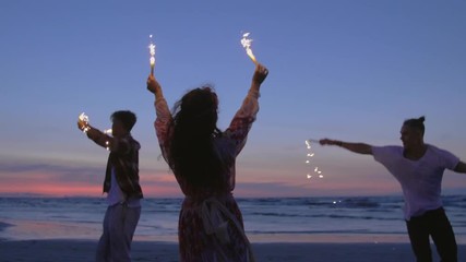 hippie friends dancing on a beach at dusk