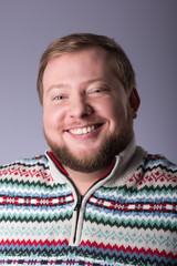 A young man with a beard, wearing a sweater. A broad smile