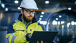 Industrial Engineer in Hard Hat Wearing Safety Jacket Uses Laptop. He Works in the Heavy Industry Manufacturing Factory with Various Metalworking Processes are in Progress.