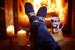 Man's feet in warm socks with large mug of hot chocolate and murshmallows near fireplace