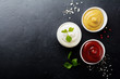 Set of three sauces - mayonnaise, mustard and ketchup in white ceramic bowls on  black stone or concrete background. Selective focus. Top view.