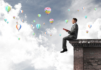 Man on roof reading book and aerostats flying in air