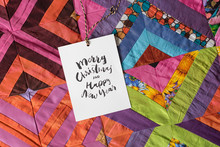 Christmas, Sewing, Present Concept. Squares Of Textile Patches Of Different Colores And Patterns Sewed In One Bright Blanket And There Is Small Greeting Card On It