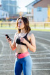 Serious female jogger looking confident. Young fitness woman listening music with headphones after training outdoors at stadium track. Girl runner listen music in earphones from smartphone.