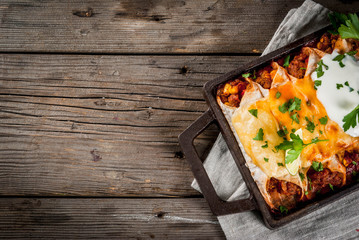 Mexican food. Cuisine of South America. Traditional dish of spicy beef enchiladas with corn, beans, tomato. On a baking tray, on old rustic wooden background. Top view copy space