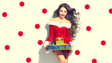 Christmas Scene. Sexy Santa. Beauty Model Girl Wearing Red Party Costume Holding Gifts