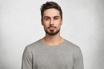 isolated shot of young handsome male with beard, mustache and trendy hairdo, wears casual grey sweat