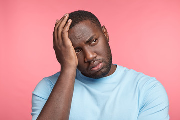 Wall Mural - Sorrorful thoughtful male with dark pure skin, keeps hand on head, thinks over his future actions, being depressed after getting failure, can`t improve situation for better, feels puzzled, frustrated