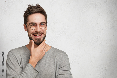 Fotografia Positive bearded thoughtful male has brilliant idea, wants to realize it, keeps hand on chin, poses against white background with copy space for your advertismet