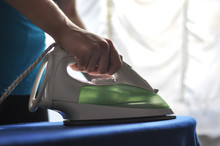 Closeup Of Woman Ironing Clothes On Ironing Board. Woman Ironing Clothes By The Window