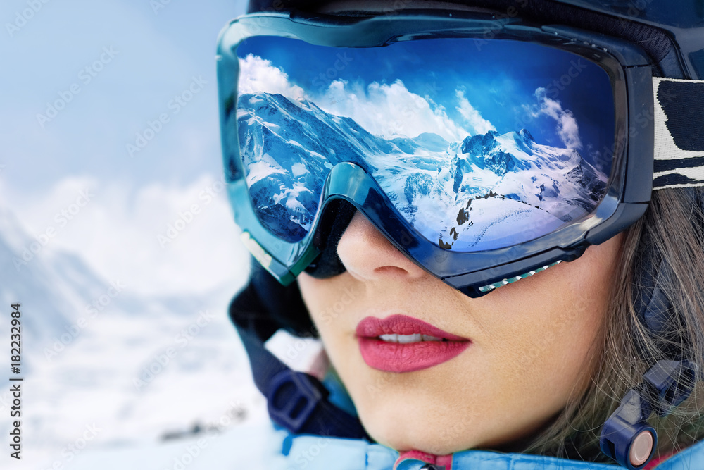 Portrait of young woman at the ski resort on the background of mountains and blue sky.A mountain range reflected in the ski mask - obrazy, fototapety, plakaty 