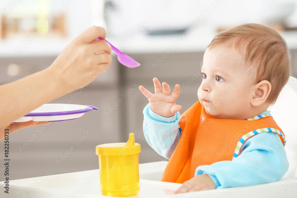 Mother feeding baby with spoon indoors