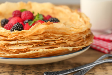 Canvas Print - Plate of delicious thin pancakes with berries on wooden table, closeup