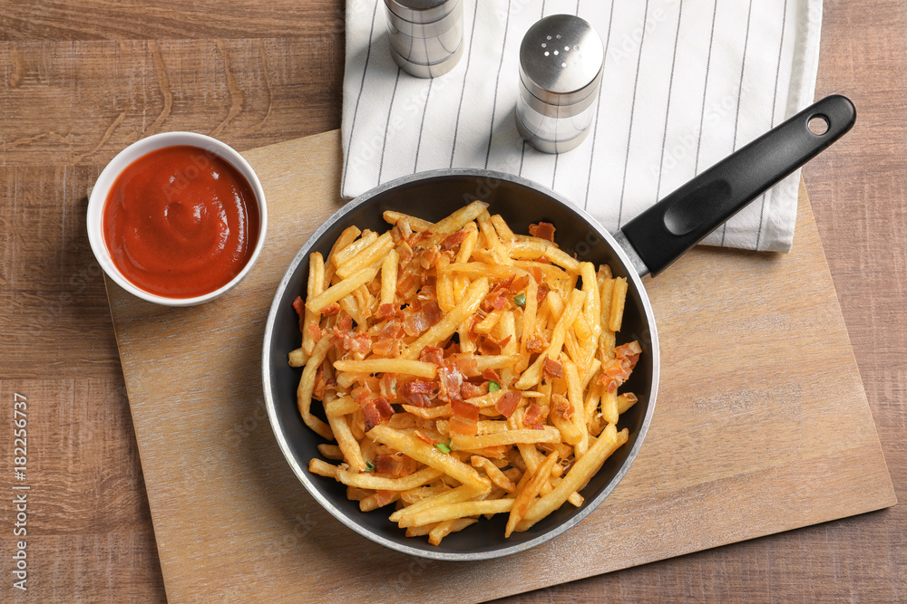 Frying pan with french fries and bacon on table