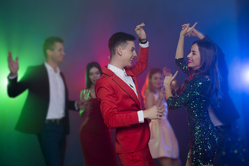 A group of young cheerful and happy friends are dancing at a party. Man and woman dancing in the foreground in front of the camera