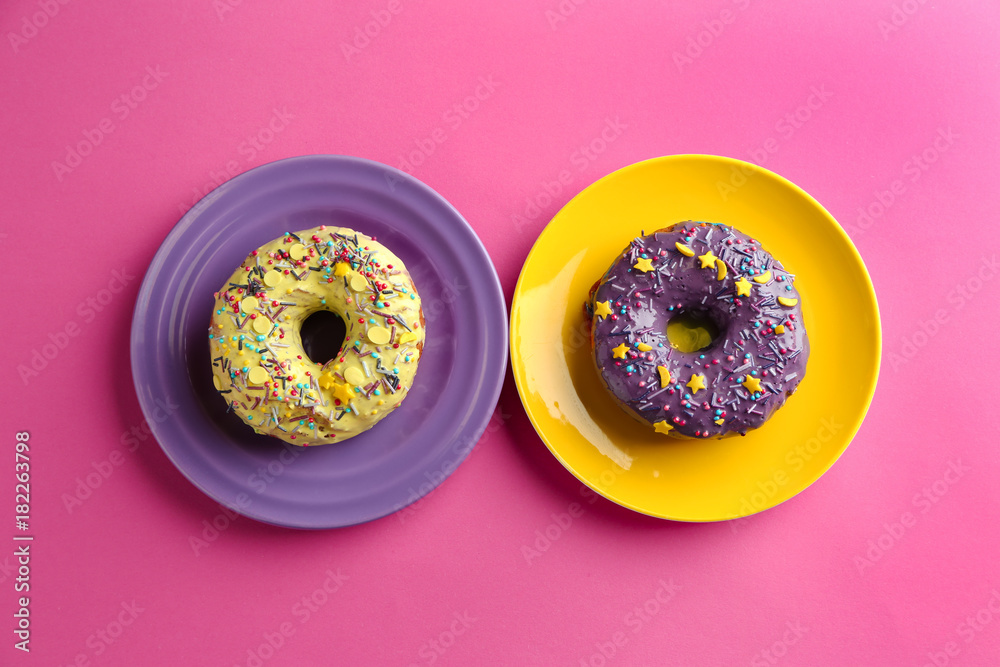 Plates with tasty glazed donuts on color background