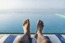 Horizontal Orientation Of Male Feet On A Sun Lounger Overlooking An Infinity Pool Towards The Ocean, With Space For Text