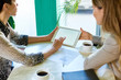 © Seventyfour - High angle view of two modern unrecognizable women  working at table in cafe using digital tablet during business meeting