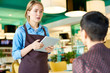 © Seventyfour - Portrait of young cafe waitress  wearing apron taking order from client using digital tablet, copy space