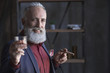 Cheer. Portrait of smiling elegant bearded old businessman tasting appetizing alcohol and keeping tobacco. Celebration concept