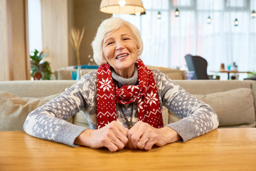 Wall Mural - Portrait of white haired senior woman smiling happily looking at camera sitting at cafe table and wearing knit scarf