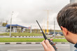 © Gribanov - Man holds a walkie-talkie in his hand and stares into the distance at a blurry road in the background, a back view