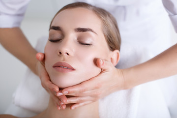 Wall Mural - Close up of masseuse hands massaging female chin and neck. Young woman closed eyes with enjoyment. Peace and comfort concept