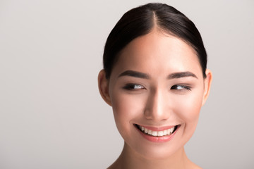 Feeling good. Close-up portrait of cheerful young asian girl with fresh and pure skin is looking aside playfully and smiling. She is expressing gladness. Isolated with copy space in the left side