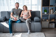 © Yakobchuk Olena - Happy family. Full length portrait of excited married couple sitting on sofa and smiling. Pregnant woman is touching her belly with joy