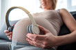 Low angle close up of happy expectant mother giving listening to music to her unborn baby. Focus on headphones near big belly