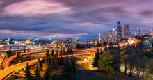 Seattle Cityscape At Dusk With Skyscrapers, Winding Highways Parks And Sports Arenas Under A Dramatic Sky.